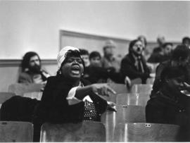 A woman speaking during a conference gathering while pointing towards the stage