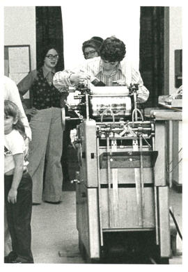 Amazon Print Shop interior view with Holly Devor (Aaron Devor) working on a press with other pers...