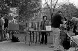 Woman stands behind registration tables with a "Vote For Peace Here" sign. Toronto, 1988.