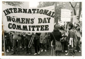 Women marching in the street, some playing musical instruments and others  holding "International...