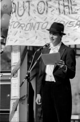 Close-up view of a man wearing a black suit and a fedora speaking at the TDN demonstration, Toron...