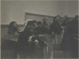 A woman speaking during a conference gathering while pointing towards the stage