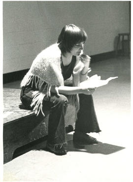 Unidentified woman sitting on a stage and reading some poetry during a poetry reading rehearsal, ...