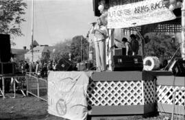 Woman speaking in a gazebo at a demonstration surrounded by Toronto Disarmament Network banners