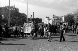 A crowd of people protesting, holding a "He is the Peace Between Us Newman '87" banner. TDN demon...